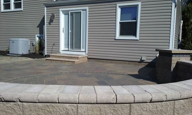 Patio with a curved retaining wall, leading to a house with a sliding door and windows.