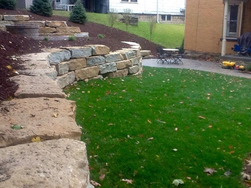 Stone retaining wall, steps, and green lawn in a backyard setting.