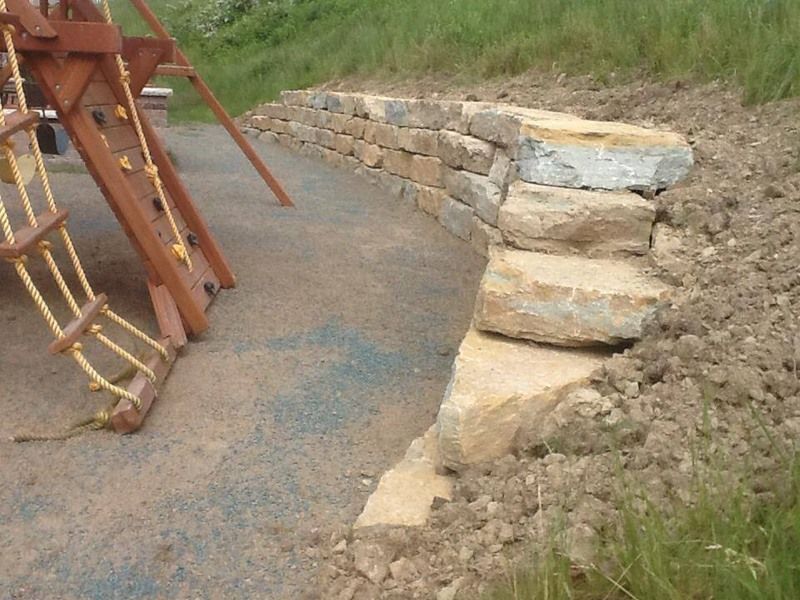 Stone retaining wall with steps next to a playground structure and grass.