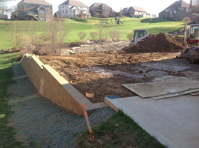 Construction site: retaining wall being built in a residential backyard, heavy equipment present.