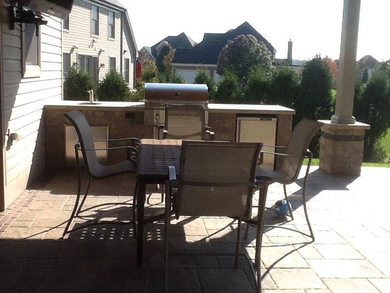 Patio with grill, table, chairs, and built-in counter. Sunny day, residential setting.