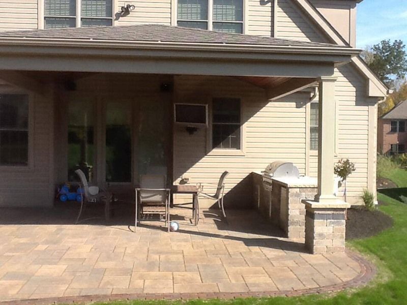 Patio with stone pavers, outdoor kitchen, covered seating area, and grass lawn.