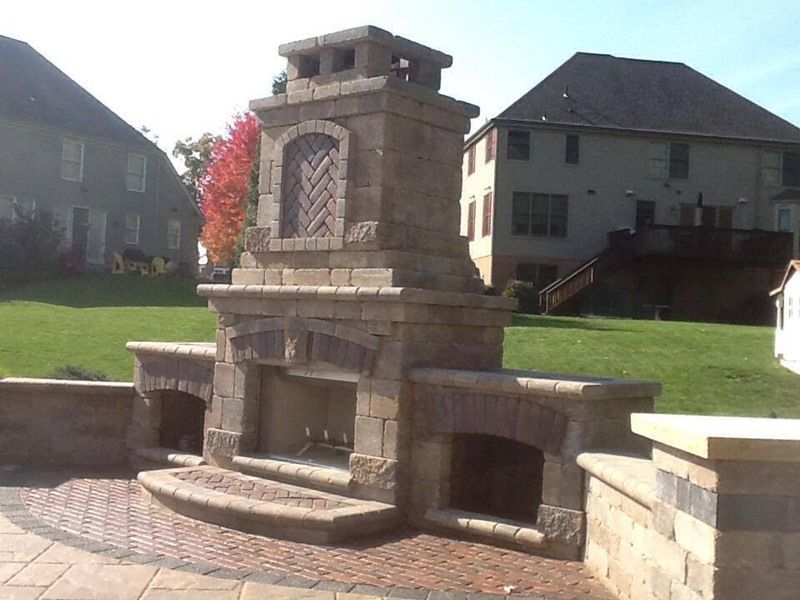 Outdoor stone fireplace with brick accents and side storage, in a backyard setting.