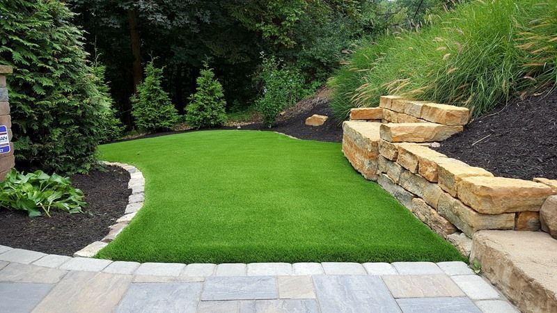Artificial turf lawn bordered by landscaping and stone retaining wall.