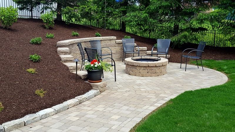 Brick patio with fire pit, seating, and terraced landscaping on a hillside.