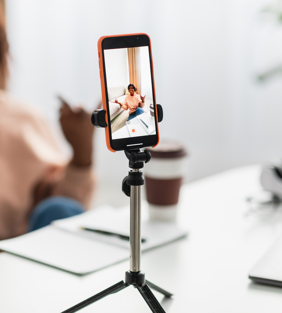 A cell phone on a tripod taking a picture of a woman sitting on a couch