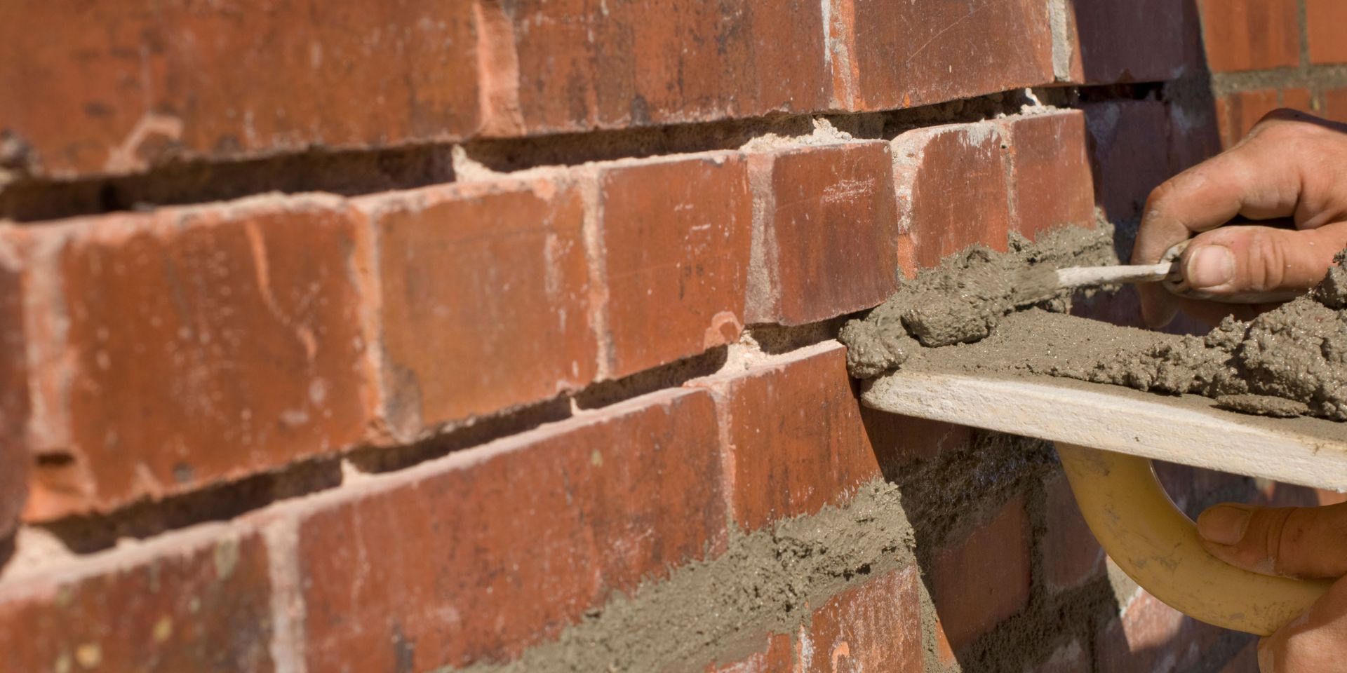 A person applies mortar to a brick wall with a trowel.