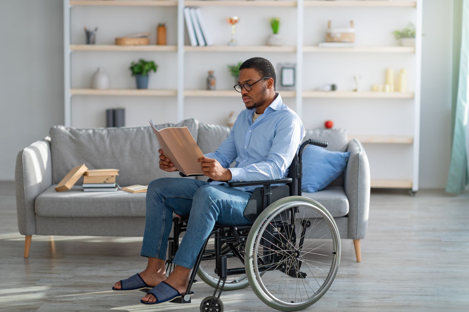 Man in wheelchair reading papers in a living room, seated in front of a gray couch.