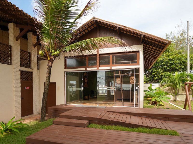 Prédio com rampa de acesso, deck de madeira, grandes portas de vidro e uma palmeira.