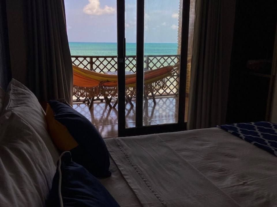 Quarto com vista para uma varanda com rede e vista para o mar.