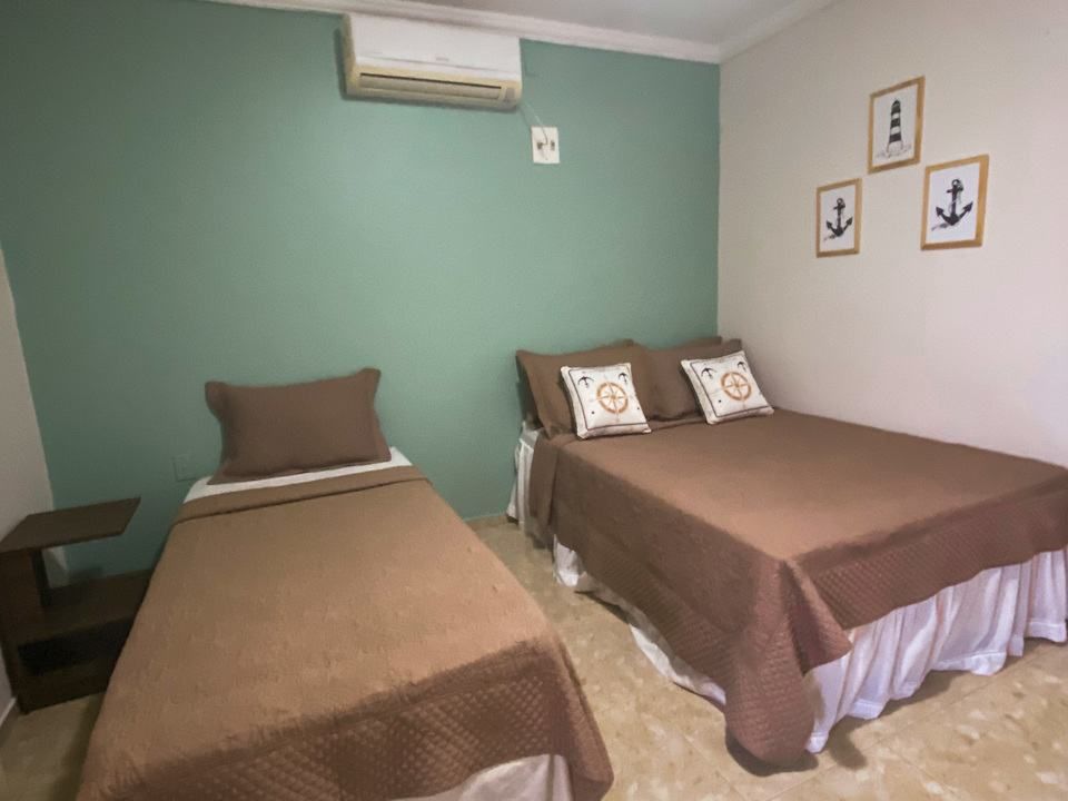 Quarto com duas camas. Roupa de cama marrom, saia de cama branca. Paredes verdes e brancas, decoração náutica.
