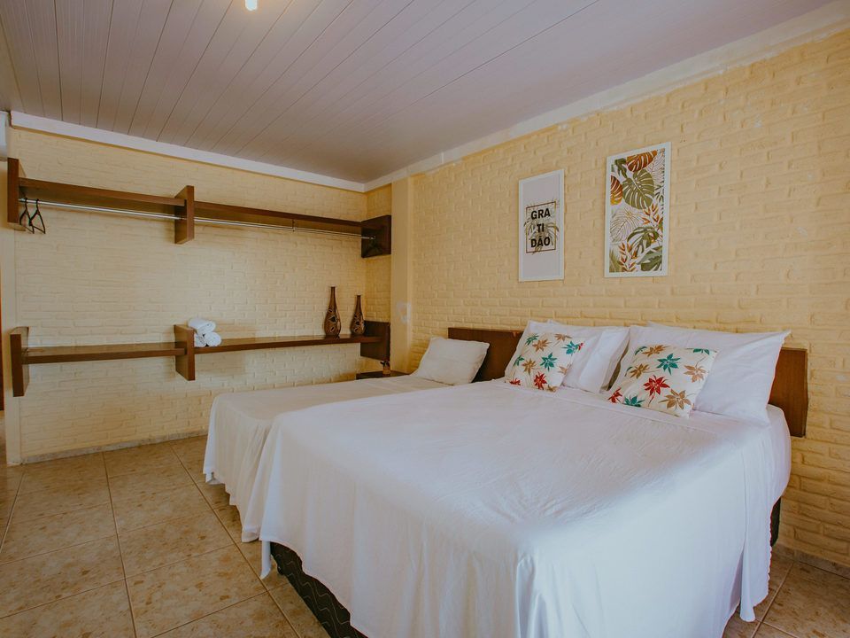Quarto com uma cama de casal e uma cama de solteiro, paredes amarelas e obras de arte.