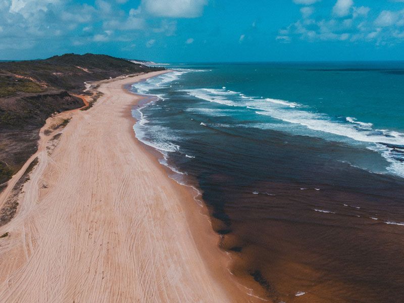 Praia de areia ao longo de um oceano azul sob um céu azul.