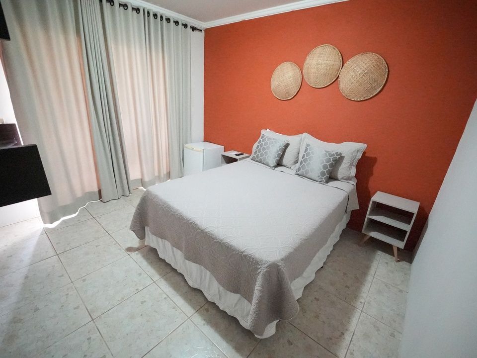 Quarto com parede laranja, cama, mesas de cabeceira, decoração de parede e cortinas.