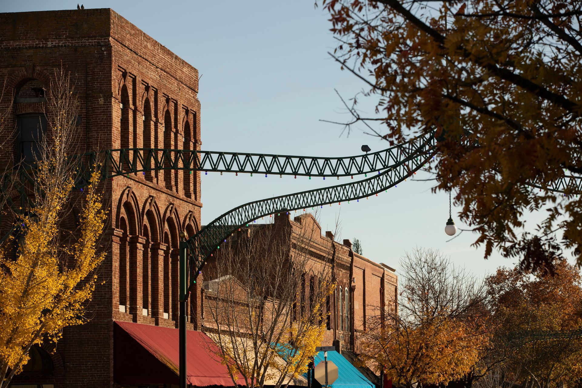 Brick buildings with a curved steel skybridge over autumn trees and colorful tents below