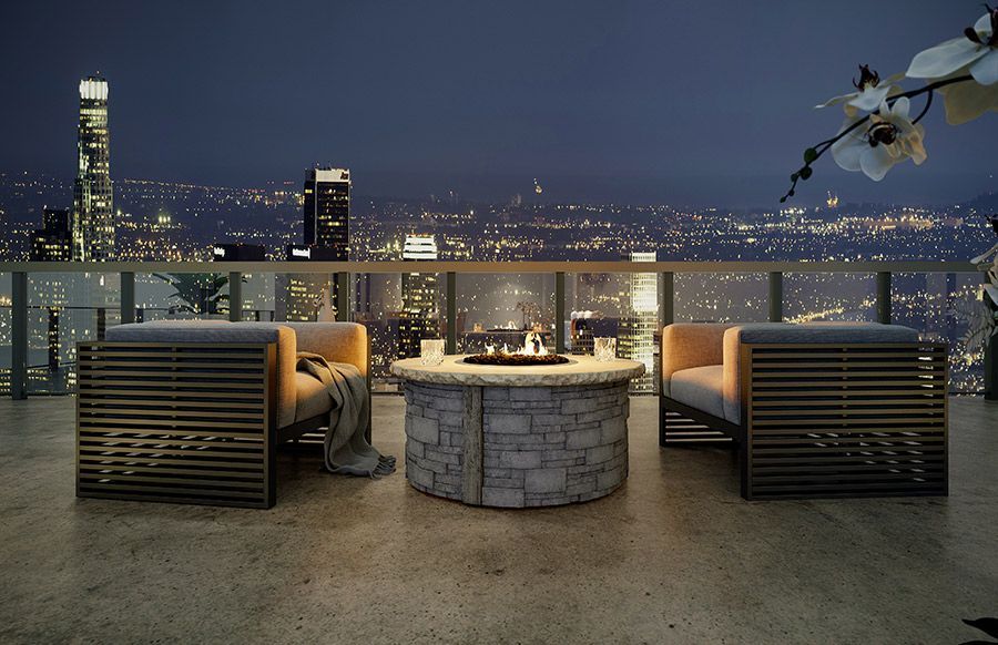 Two chairs are sitting around a fire pit on a balcony overlooking the city at night.