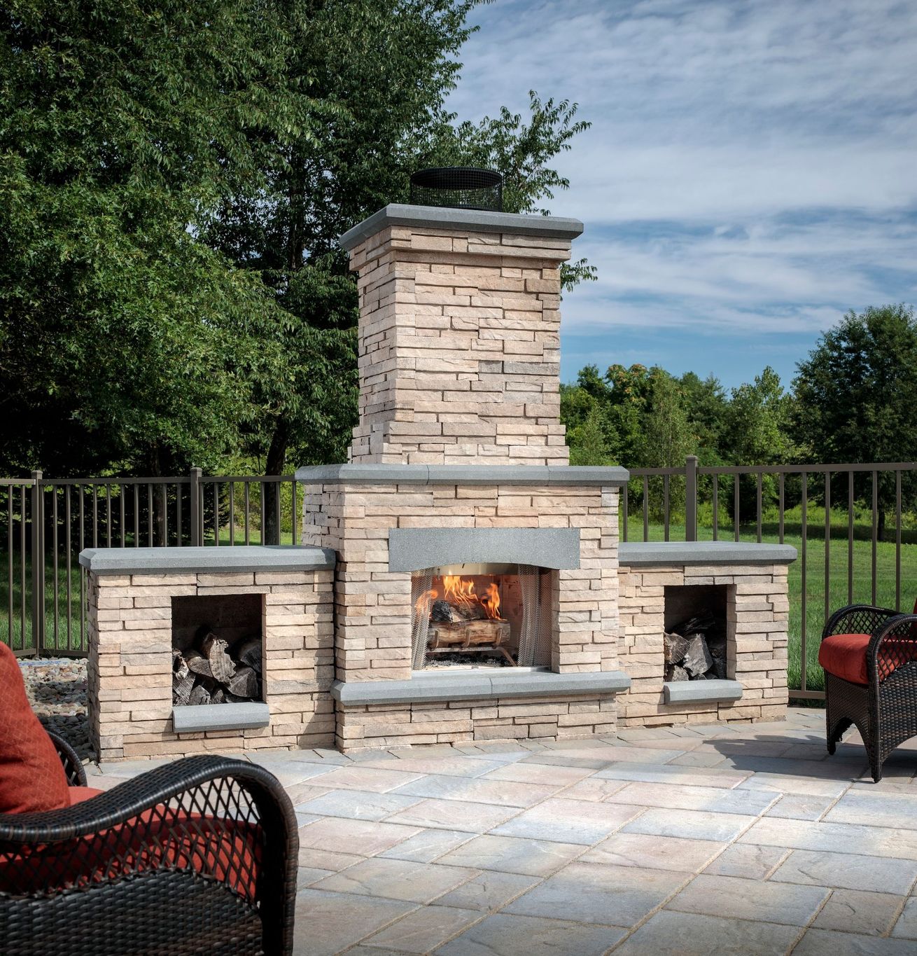 A brick fireplace is surrounded by chairs and a fence