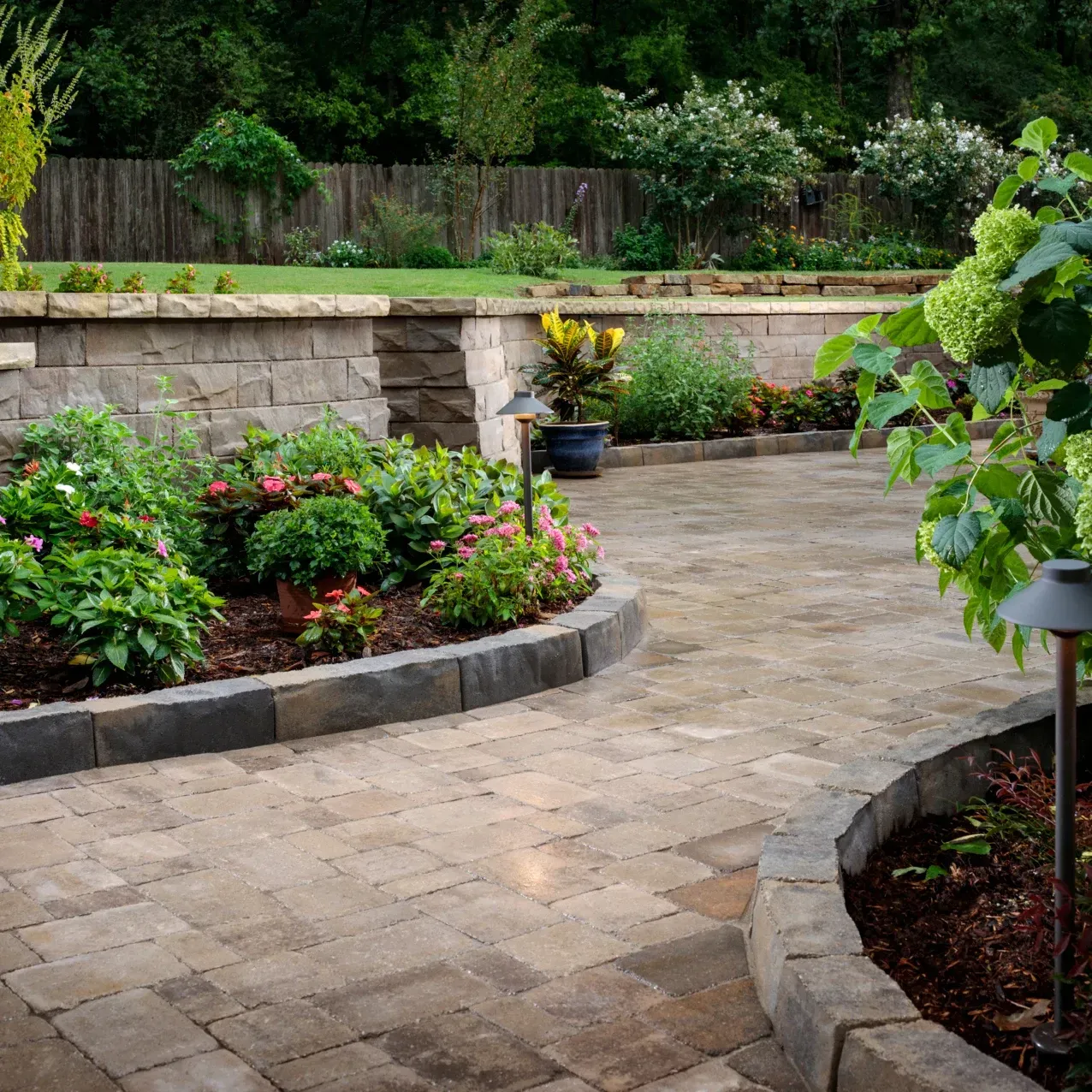 A brick walkway surrounded by flowers and trees
