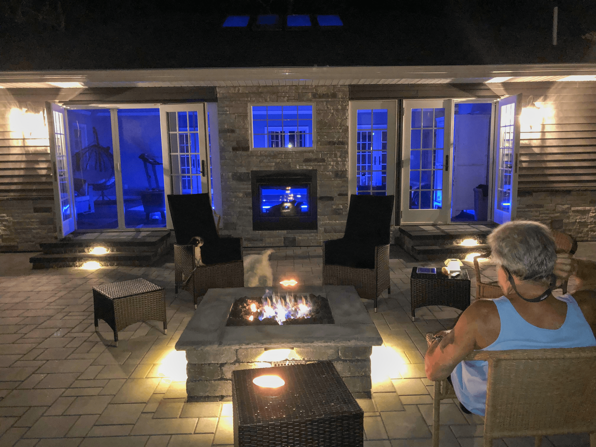 A woman is sitting in front of a fireplace on a patio at night.