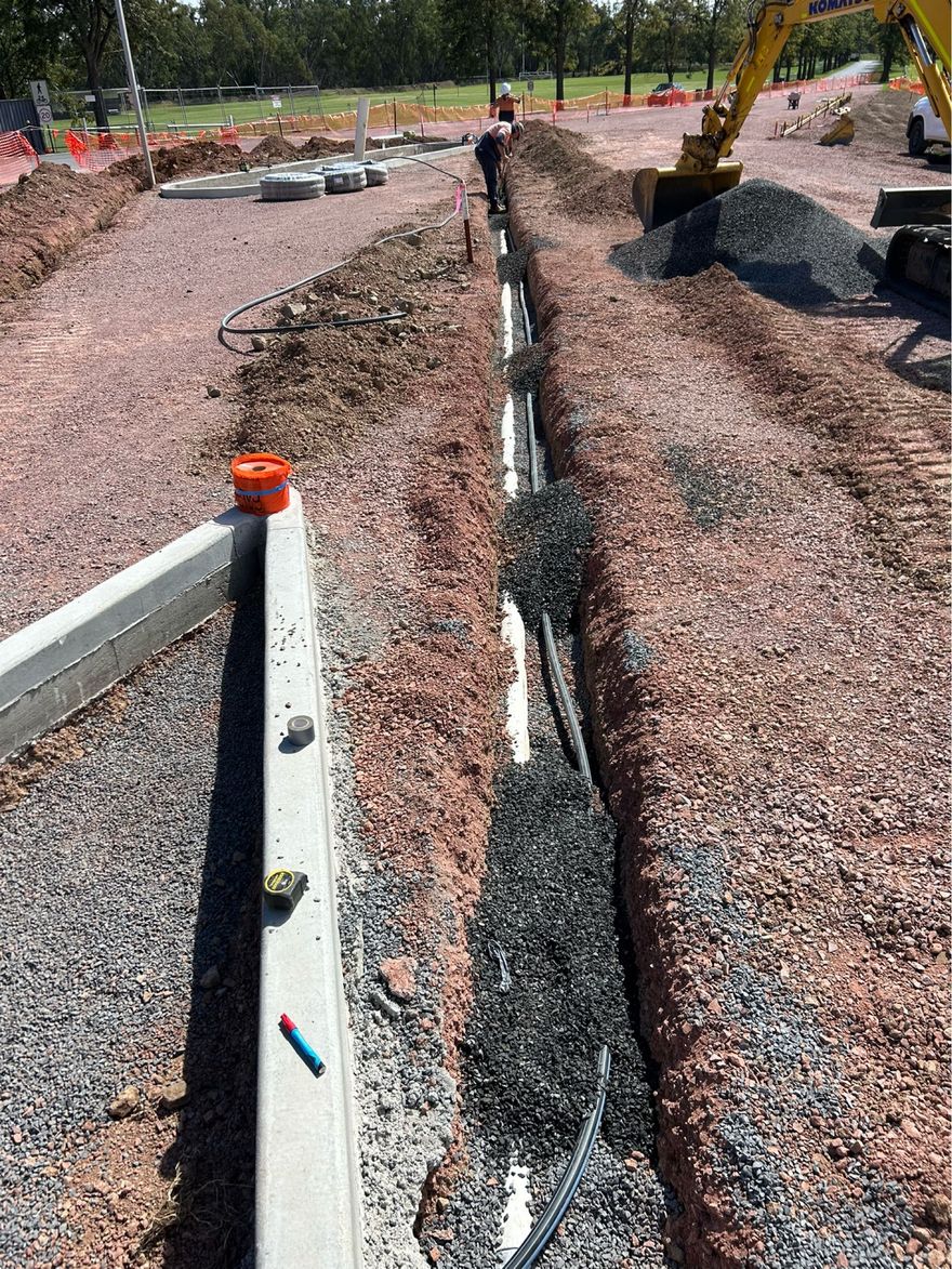 Plumber working on a gray PVC pipe connection near a concrete wall; red overalls are visible.Orange NSW