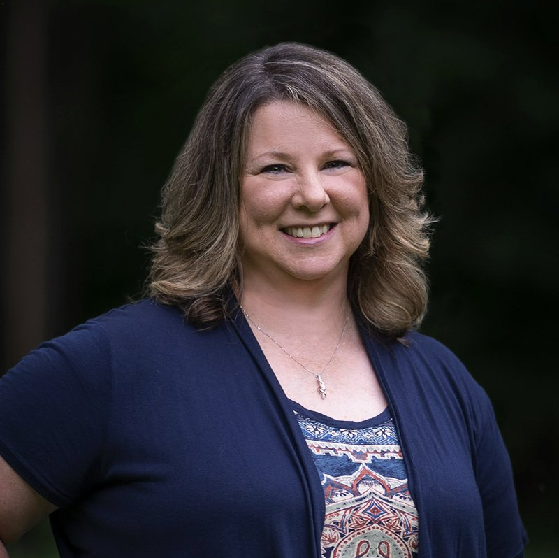 A woman in a blue shirt and cardigan is smiling for the camera.