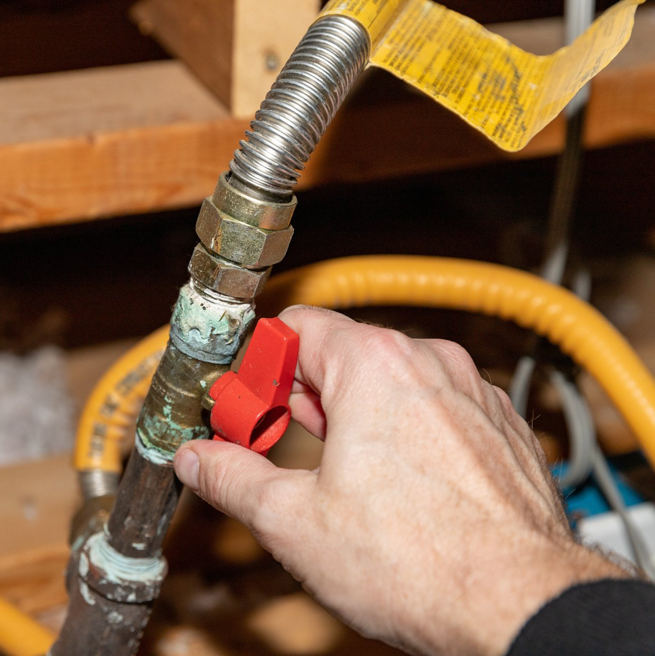 A person is holding a red valve on a gas pipe