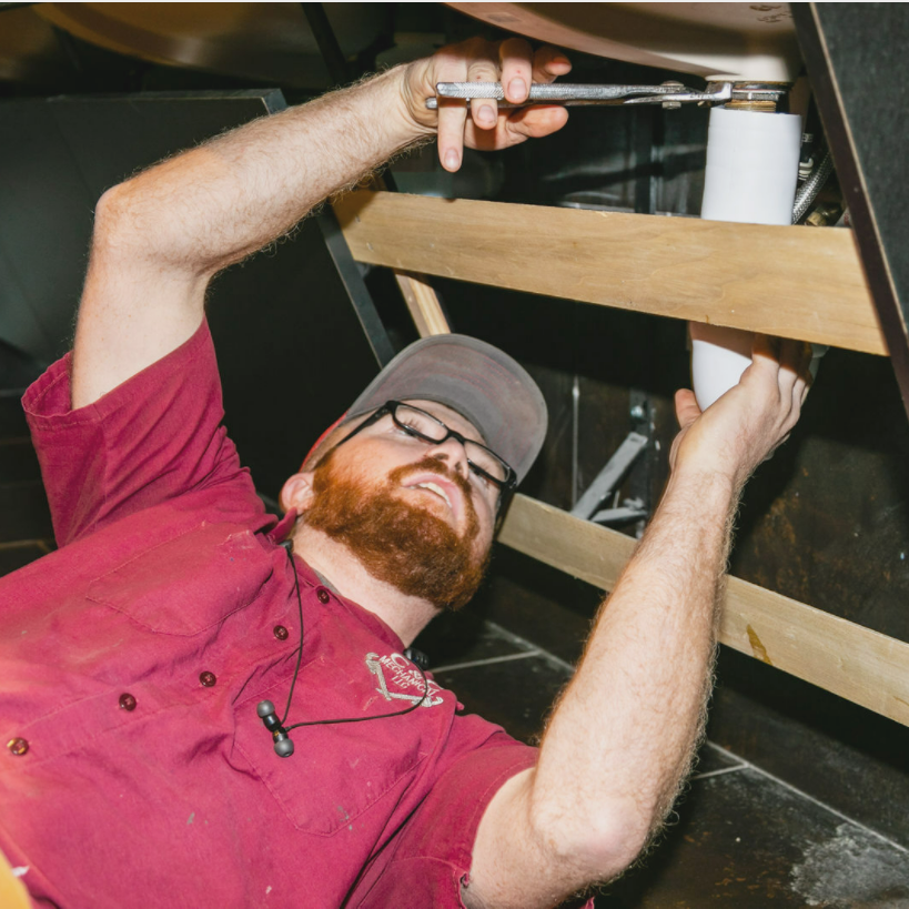 A man in a red shirt is working under a sink