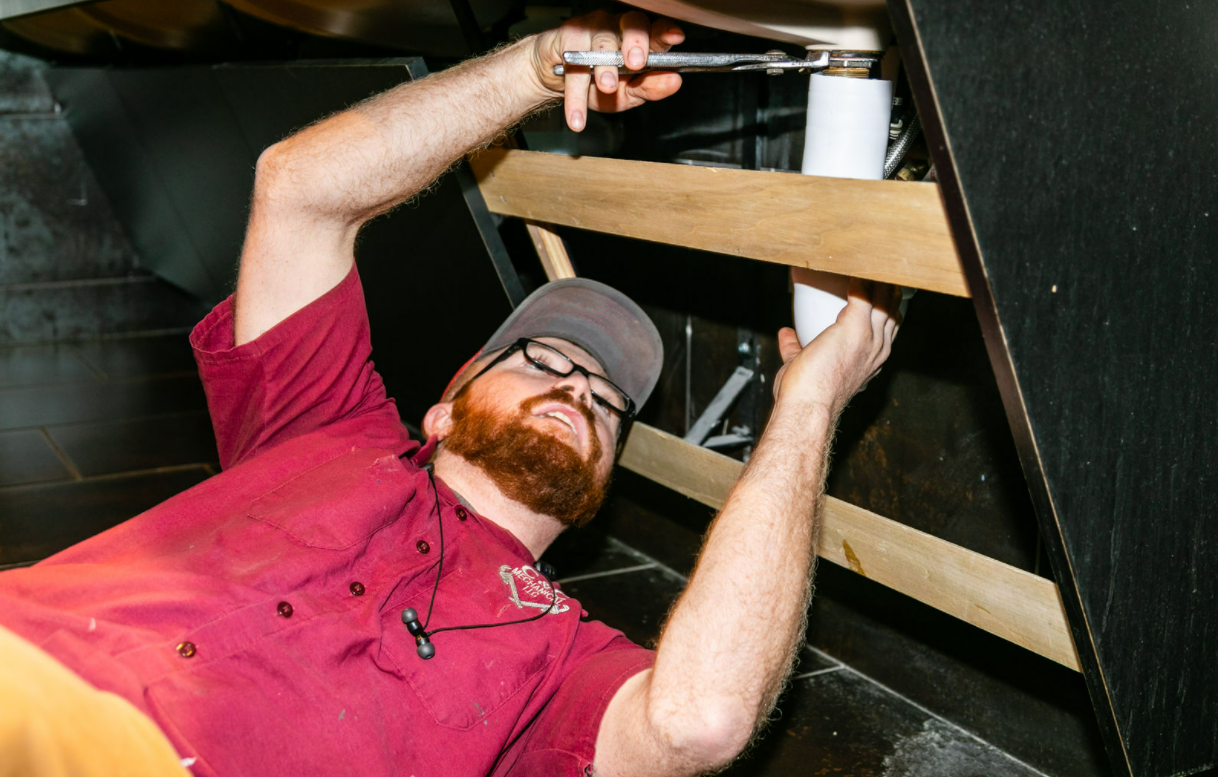 A man is laying on the floor fixing a sink with a wrench.