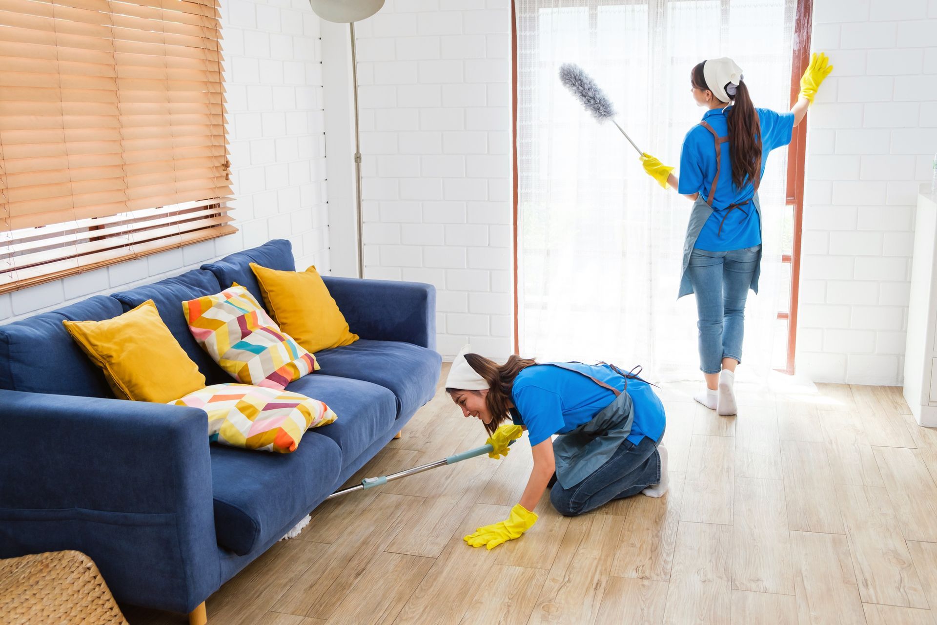 Person vacuuming a patterned rug in a brightly lit room. Yellow gloves, blue apron, and casual clothing are visible. Person vacuuming a patterned rug in a brightly lit room. Yellow gloves, blue apron, and casual clothing are visible.