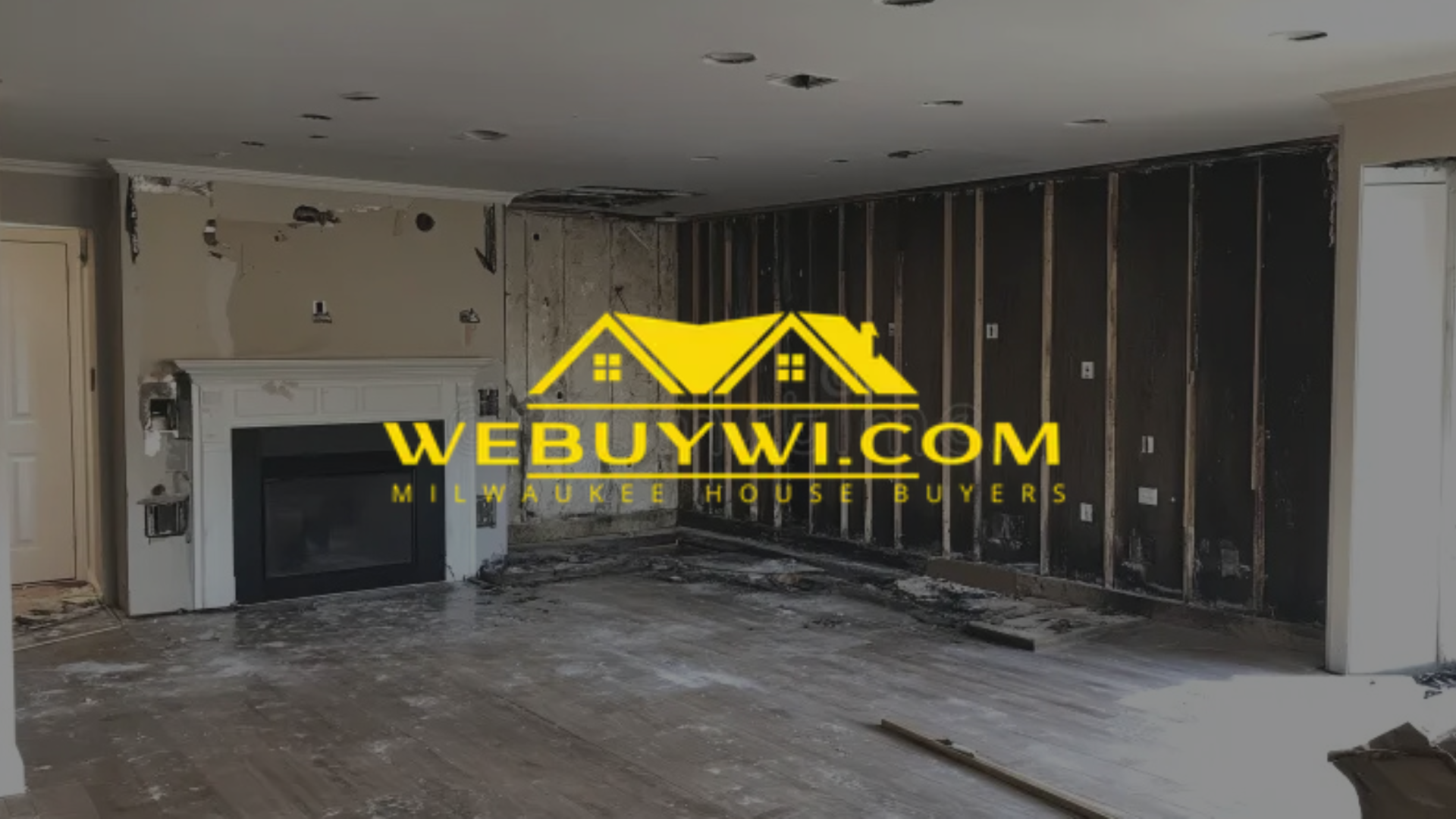 Interior of a gutted living room with a fireplace, studs exposed, and damage, likely for renovation.