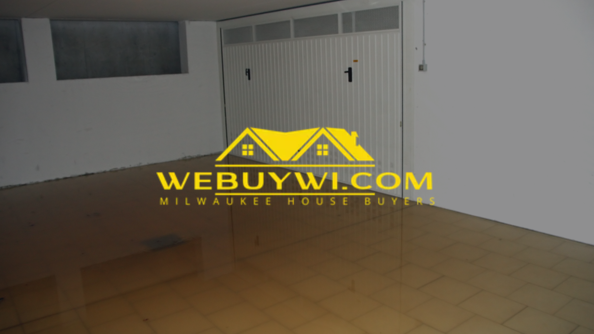 Garage interior with garage door and floor tiles, the WeBuyWI.com logo is on the floor.
