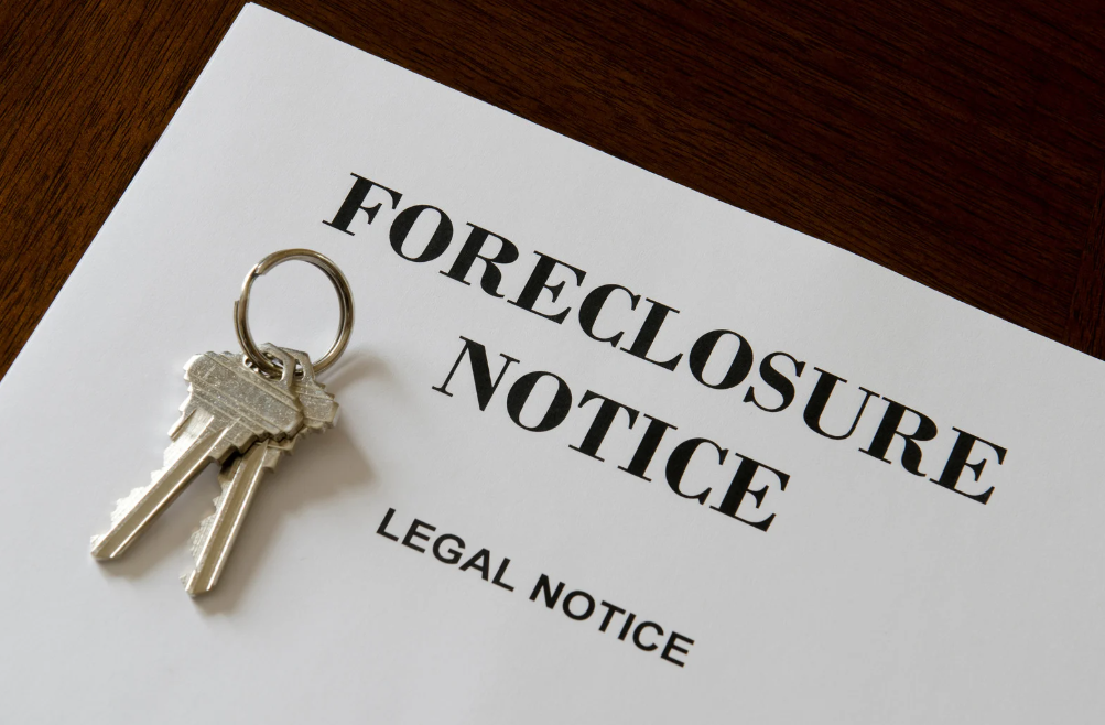 Foreclosure notice on white paper beside a keyring on a wooden surface