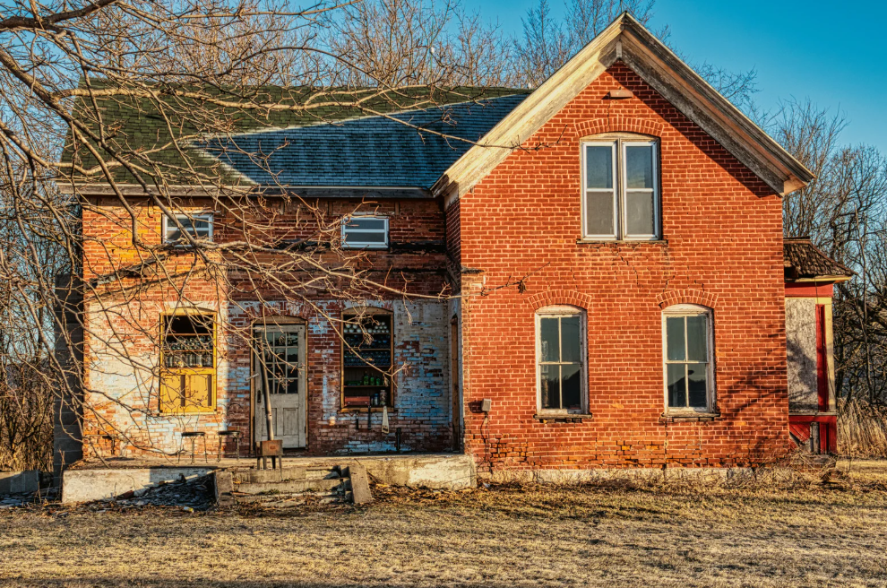 An old red brick house with a green roof is sitting in the middle of a field.