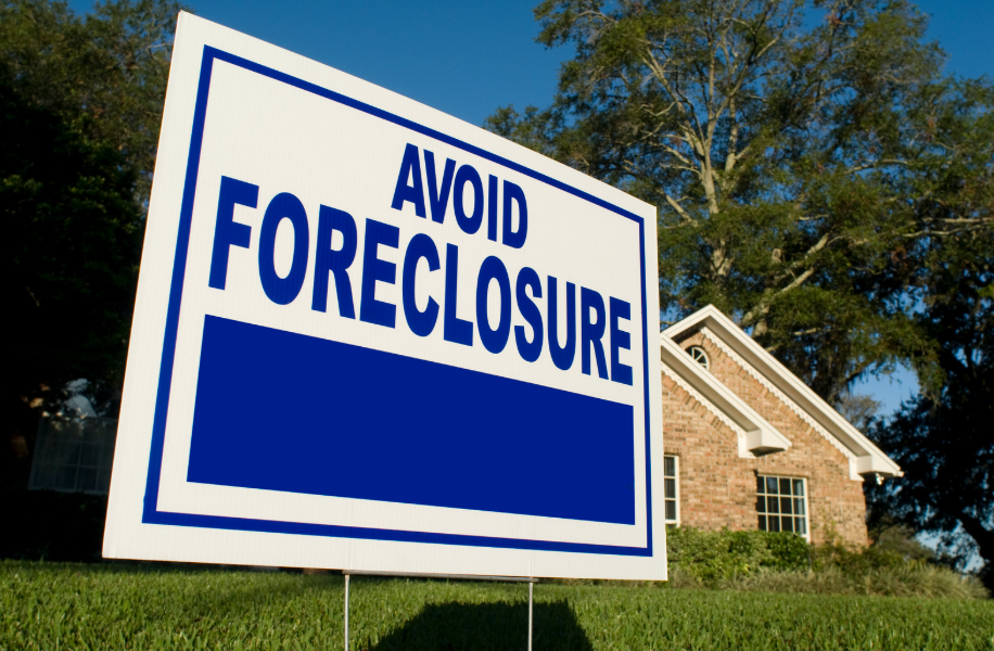 A blue and white sign that says avoid foreclosure in front of a house.