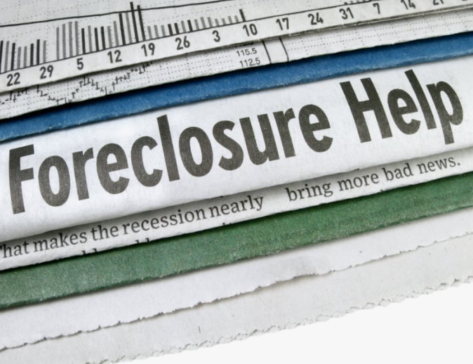 A stack of newspapers with one that says foreclosure help