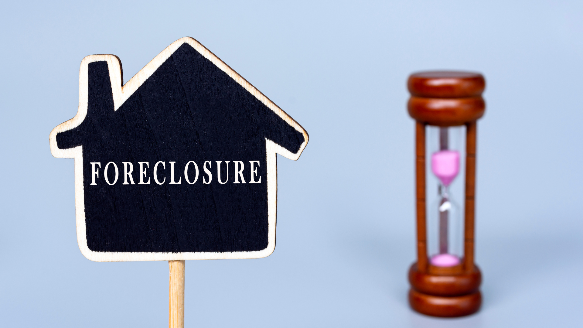 A foreclosure sign in the shape of a house next to an hourglass.
