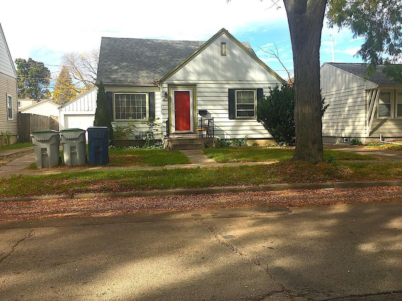 A white new berlin house with a red door and a tree in front of it.