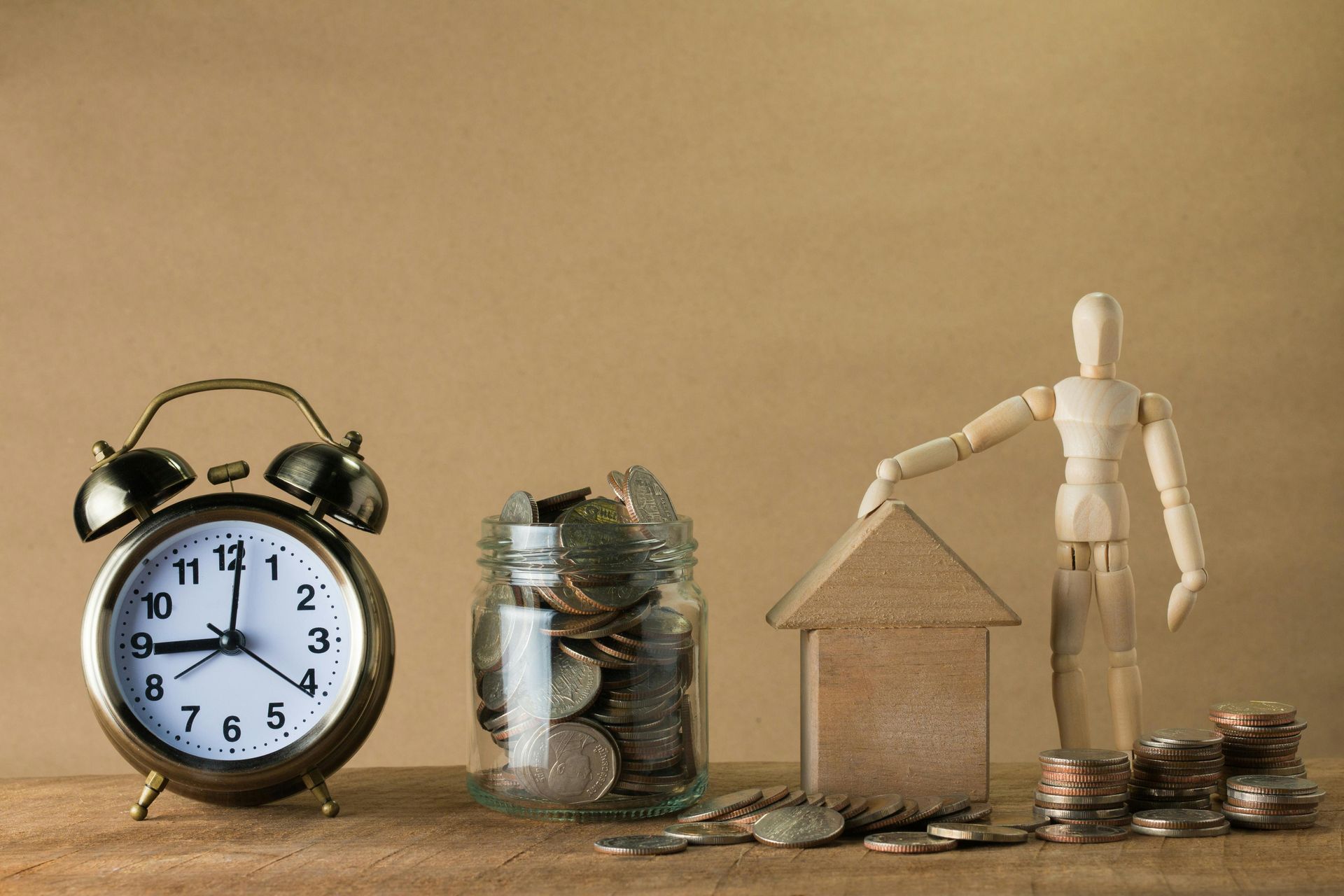Clock, jar of coins, wooden house model, and figurine symbolizing savings and time.