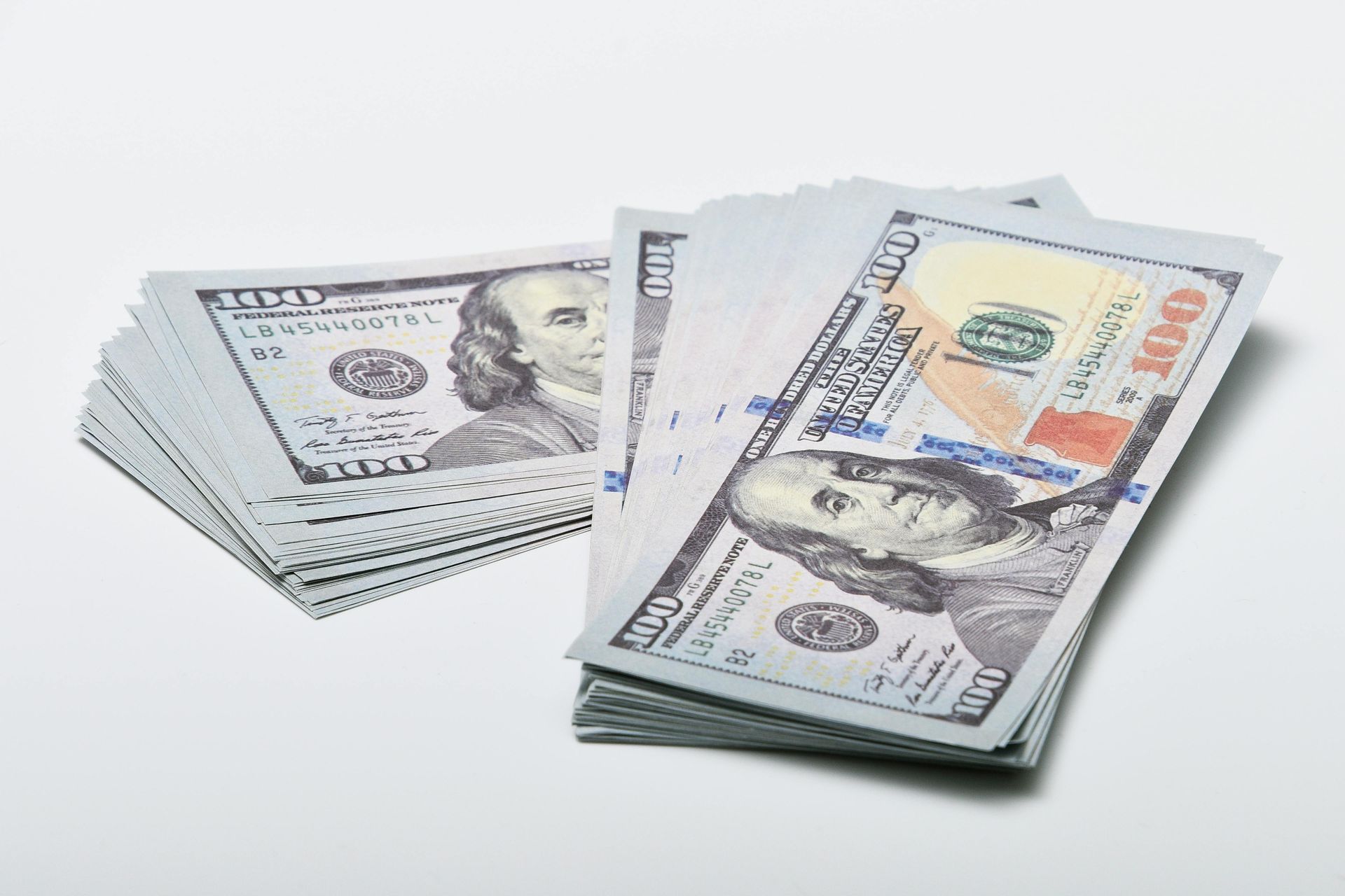 Stacks of US one hundred dollar bills on a white surface.