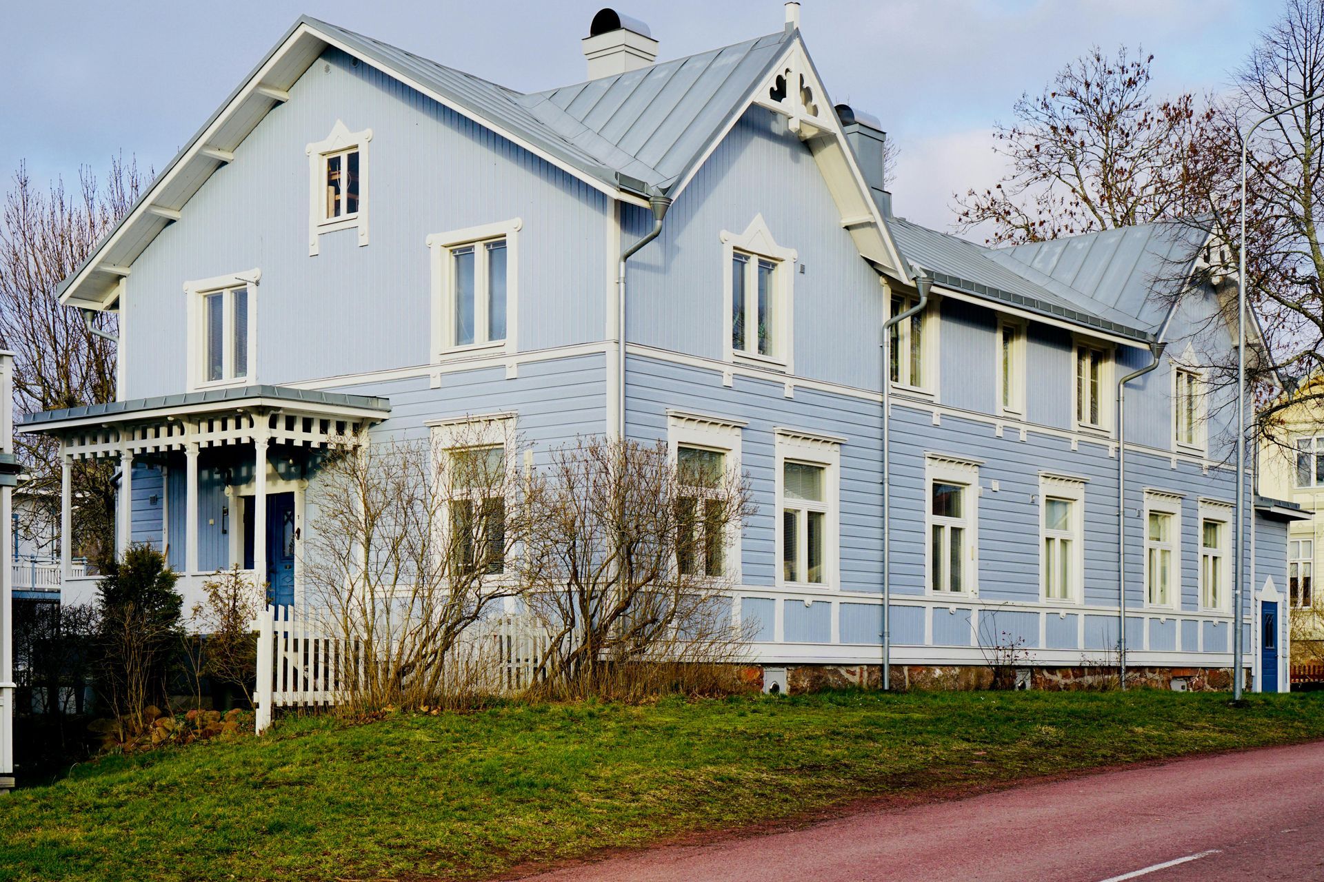Light blue two-story house with white trim. Porch, metal roof, and sparse trees in front.
