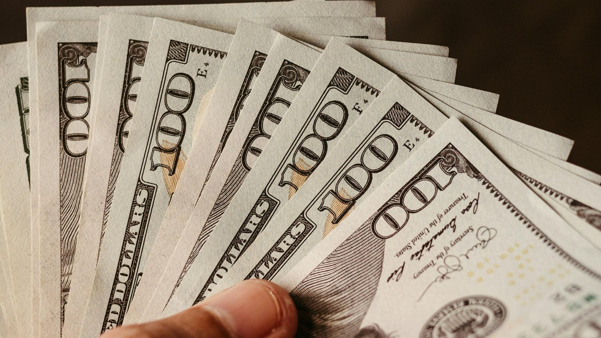 Hand holding a fan of U.S. $100 bills