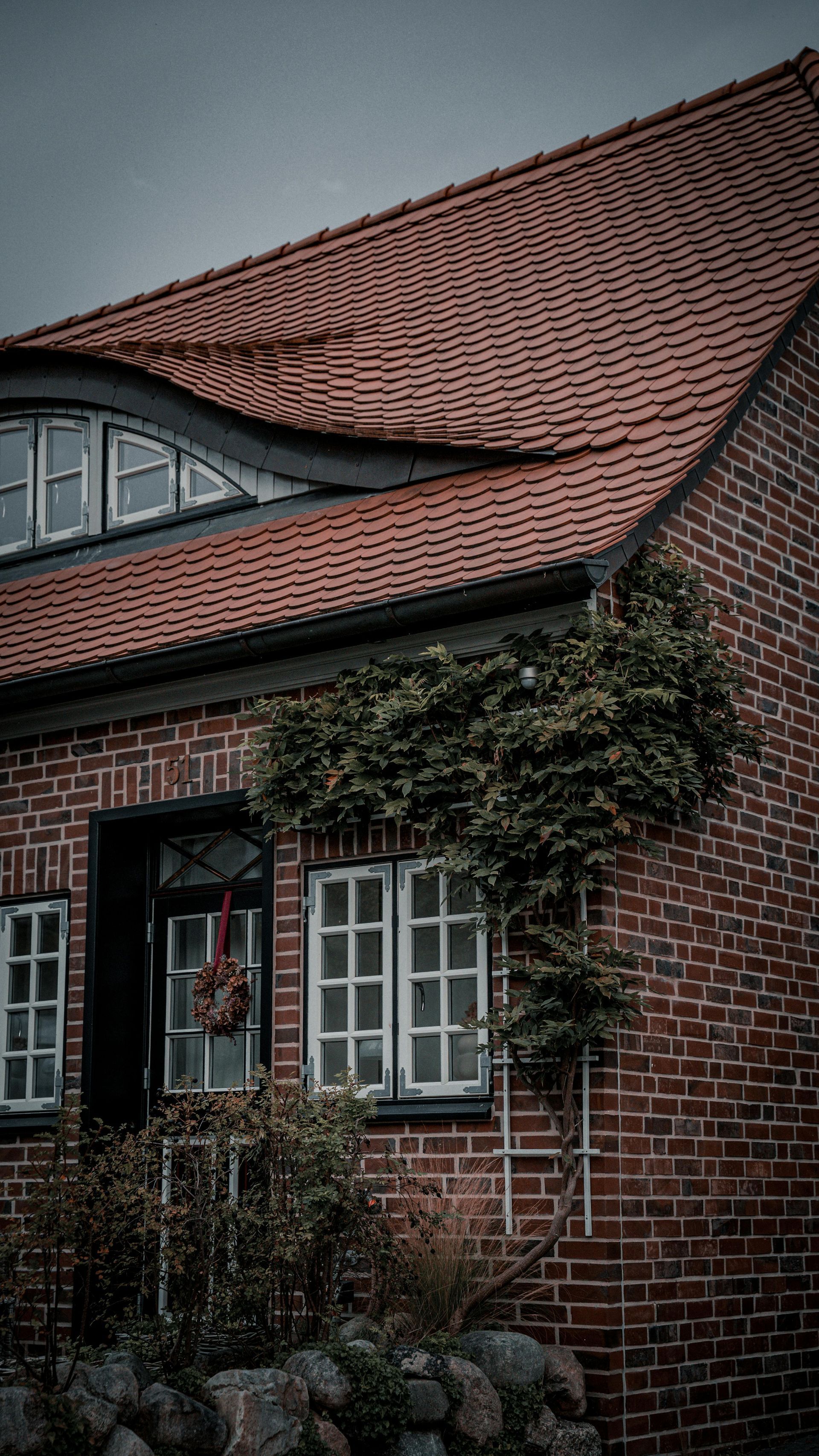 Brick house with red tiled roof, arched window, and ivy-covered wall.