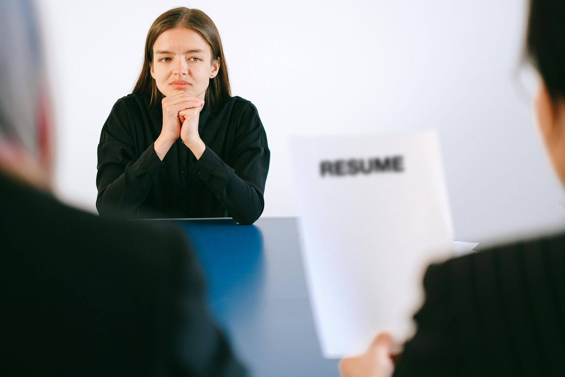 A person sits at a desk with their hands clasped while interviewers hold a document labeled