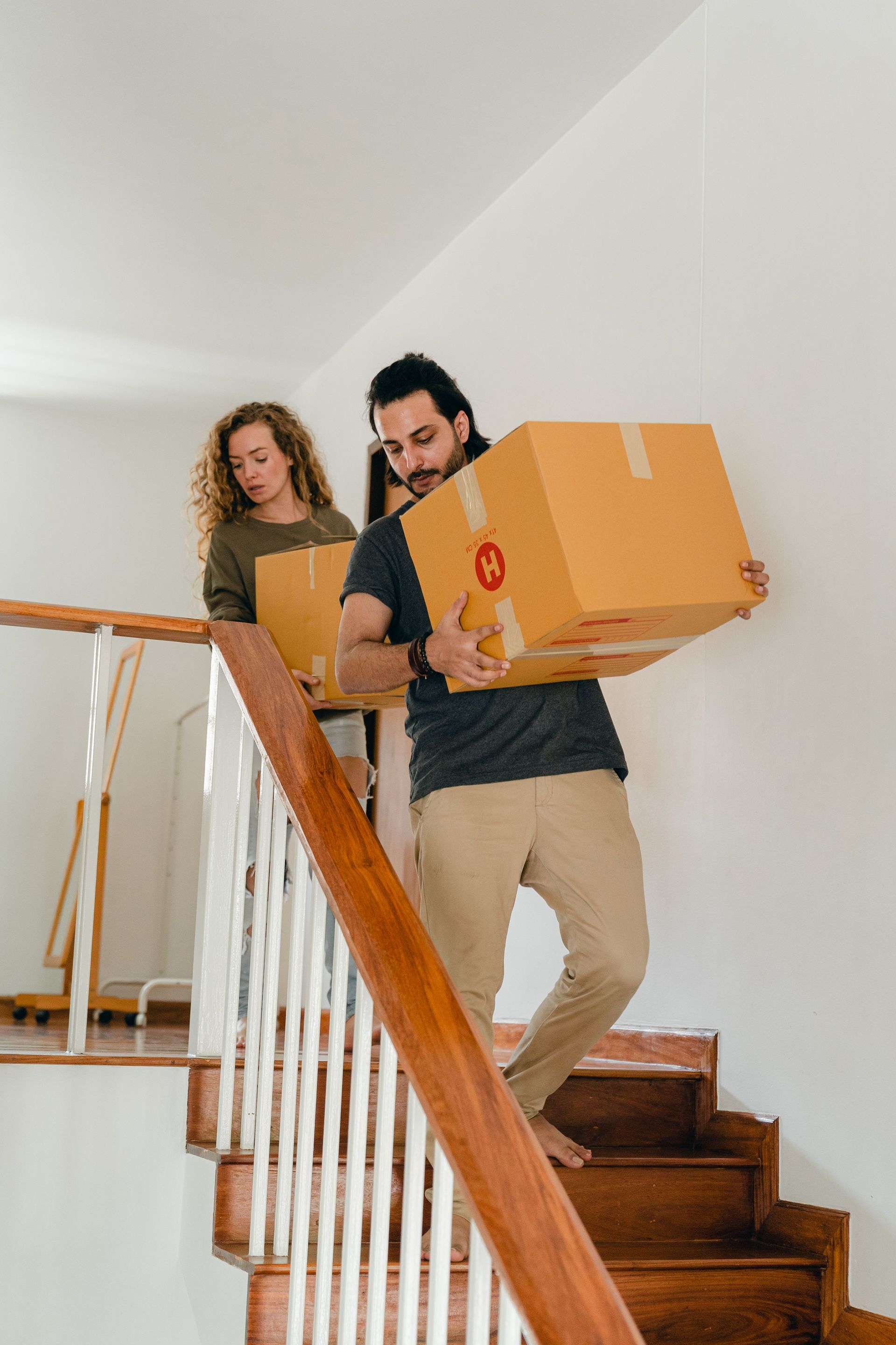 Two people carrying a large cardboard box up a staircase in a bright house