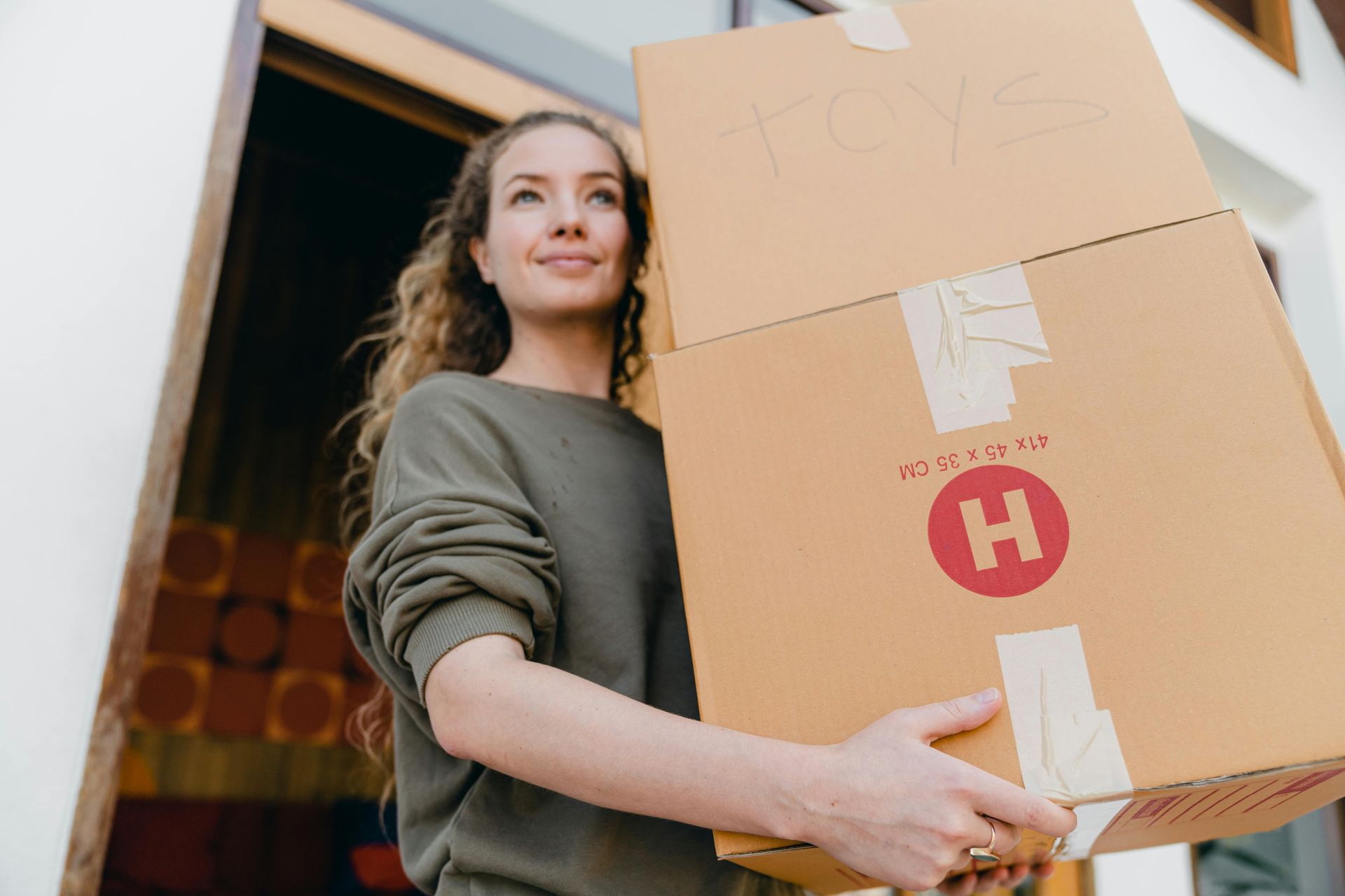 A person in a green sweatshirt holding two stacked cardboard moving boxes with a red