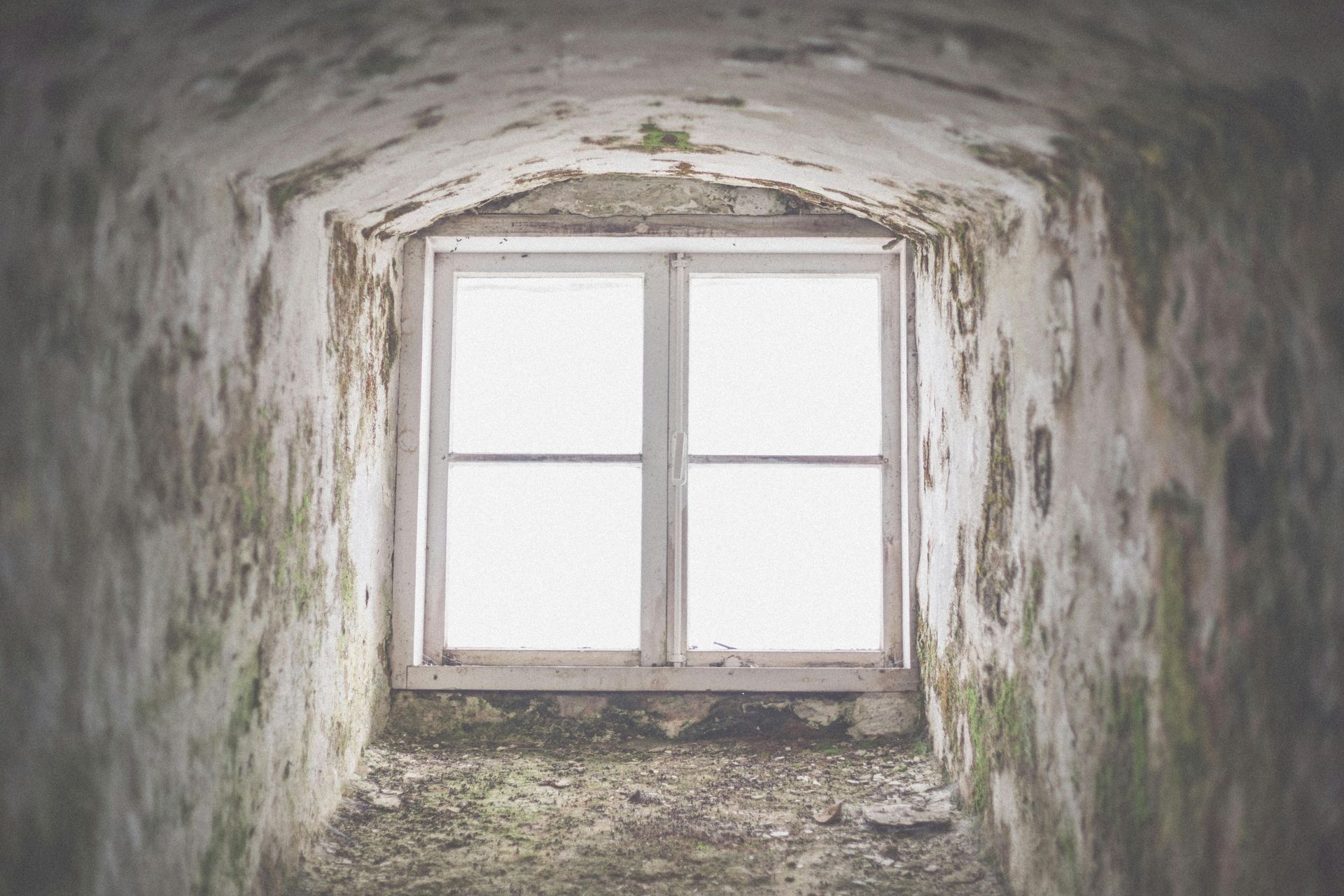 A bright window set within a deep, arched stone tunnel with walls covered in weathered, mossy textures.