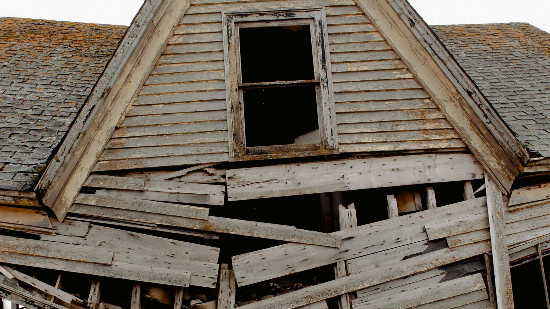 Dilapidated wooden house with a sagging roof and broken upper window