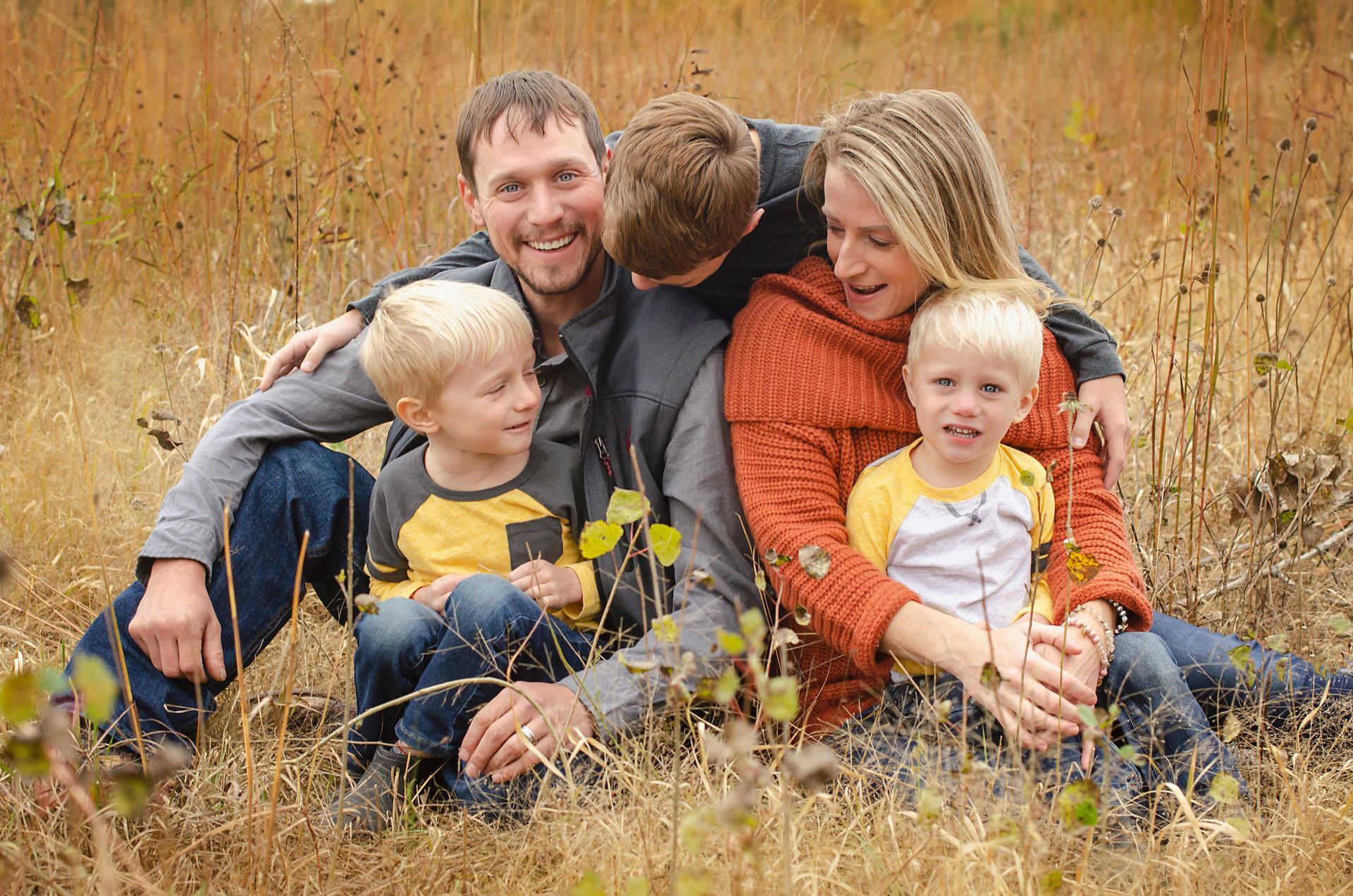Family sitting together in tall grass outdoors, smiling and cuddling in autumn colors