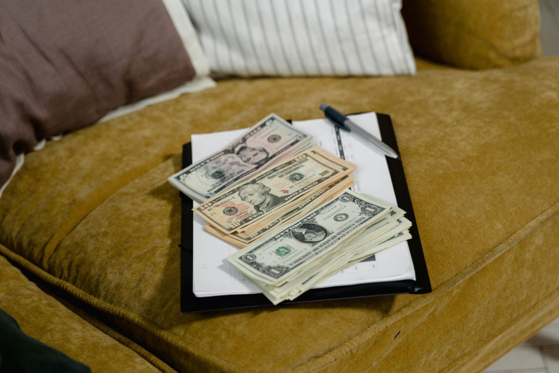 Cash on a clipboard on a mustard-colored couch
