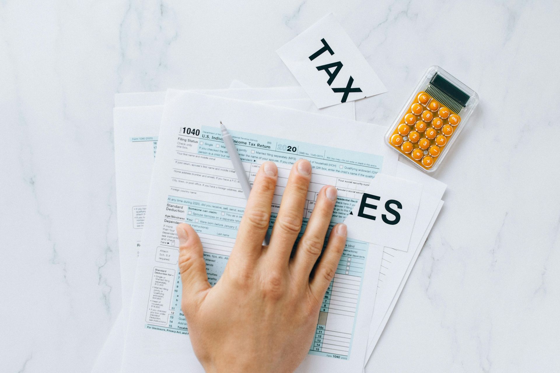 Hand resting on tax forms with calculator and